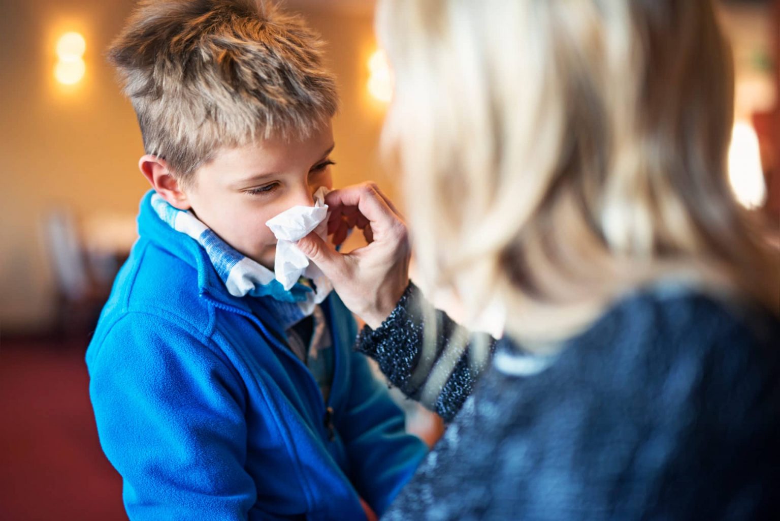 Pediatric-Allergy-symptoms A young boy experiencing allergies blows his nose into a tissue.