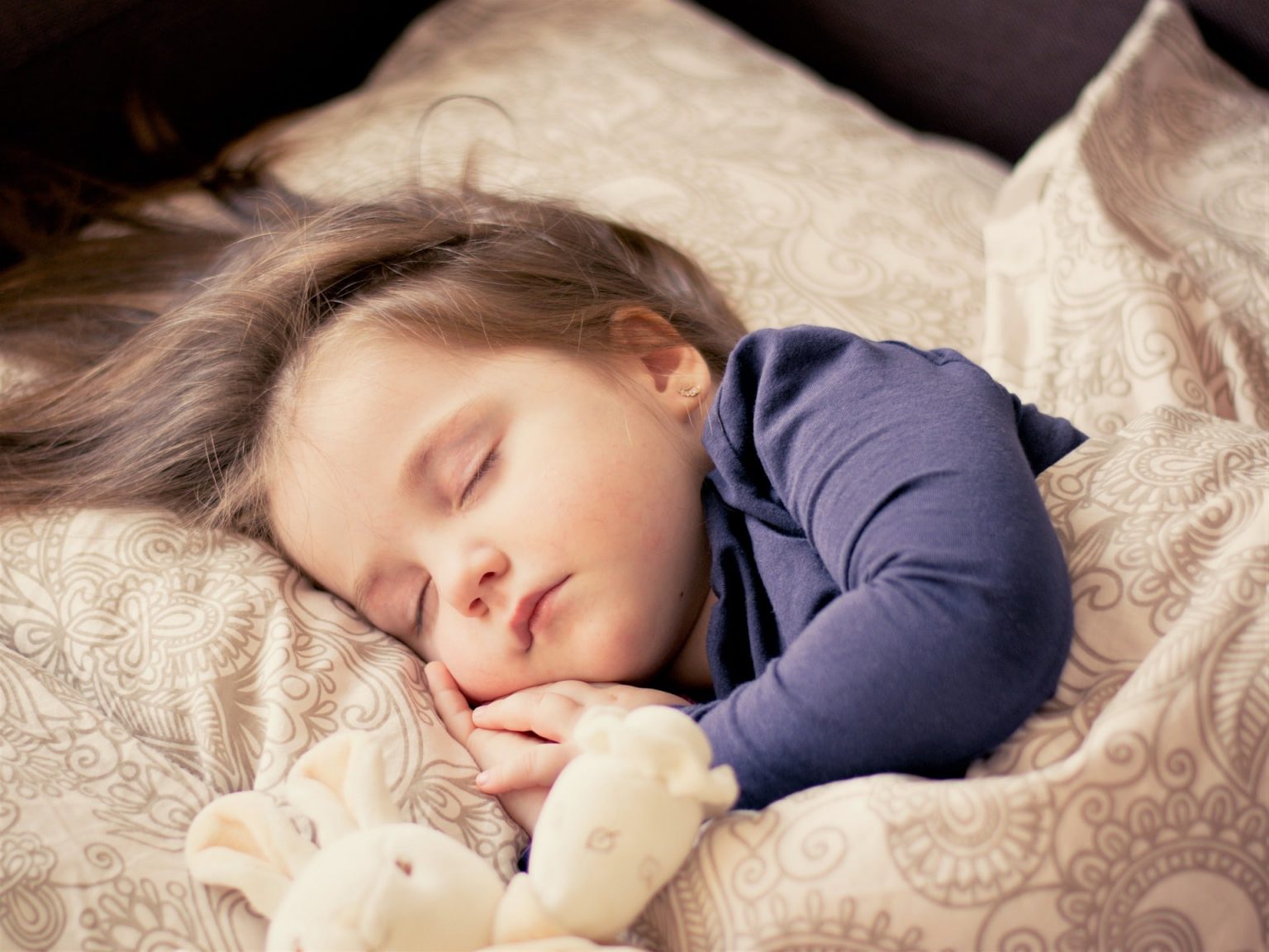 Pediatric-snoring-treatment A female toddler sleeping in bed with a stuffed animal.